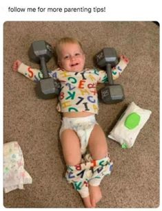 a baby laying on the floor with two dumbbells