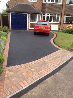 a red car is parked in front of a brick driveway with a blue garage door