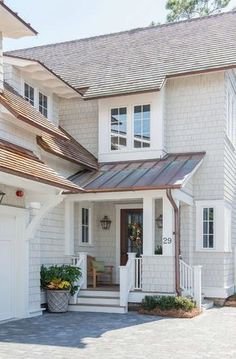 a white house with a metal roof and some plants on the front porch in front of it