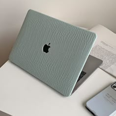 an apple laptop computer sitting on top of a white table next to a cell phone