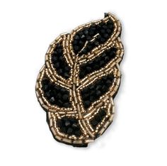 a black and gold brooch that is on a white surface with some beads around it