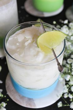 a glass filled with ice and a lime wedge on top of it next to some flowers