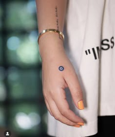 a woman's hand with an evil eye tattoo on her left wrist and orange nail polish