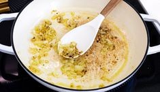 a wooden spoon in a pot filled with onions and seasoning on the stove top