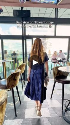 a woman in a blue dress walking into a room with lots of chairs and tables