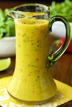 a pitcher filled with yellow liquid sitting on top of a wooden table next to lettuce