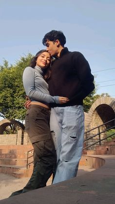 a man and woman standing next to each other in front of a bridge with trees