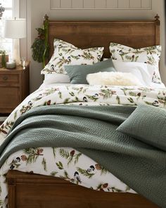 a bed with green and white comforter next to a night stand in a bedroom