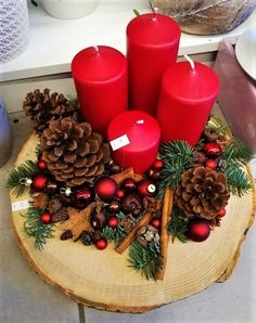 three red candles sitting on top of a wooden table next to pine cones and christmas decorations