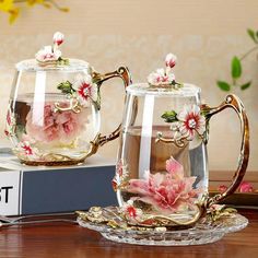 two glass teapots with flowers in them on a table next to a box