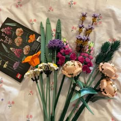 flowers are laid out on a bed next to an open book and some fake flowers