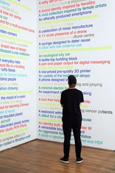 a man standing in front of a wall with words written on it and behind him is a wooden floor