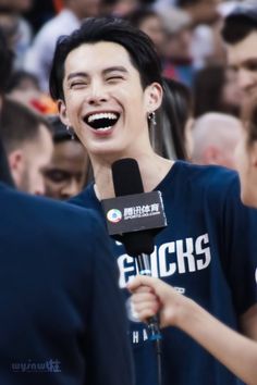 a man holding a microphone and laughing while standing in front of a crowd with other people