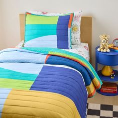 a child's bedroom with colorful bedding and toys on the side table next to it