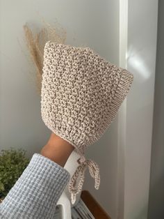 someone is holding their hand up against the wall with a crocheted hat on it