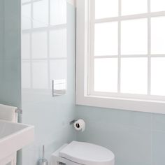 a white toilet sitting next to a bathroom sink under a window in a blue tiled room