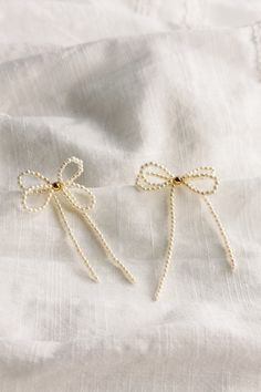 The Tarah Cream Pearl Bow Dangle Earrings, where timeless elegance meets modern sophistication. Crafted with meticulous attention to detail, these earrings exude charm and grace, perfect for any occasion. Each earring boasts delicate mini cream pearls, evoking a sense of refined beauty. A single shimmering gold pearl detail adds a touch of opulence, creating a captivating contrast against the creamy backdrop. The charming earring bow-shaped design, a symbol of femininity and grace. Whether paire Dainty White Pearl Earrings For Party, Feminine White Pearl Earrings For Evening, Feminine Pearl Earrings For Evening, Feminine Pearl White Pearl Earrings For Party, Cream Pearl Drop Jewelry, Feminine Evening Pearl Earrings, Cream Dangle Jewelry For Party, Cream Earrings For Party, Elegant Cream Earrings For Formal Occasions