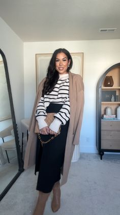 a woman standing in front of a mirror wearing boots and a coat over her shoulders