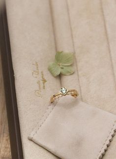 an engagement ring sitting on top of a white piece of cloth next to a green leaf