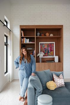 a woman standing in front of a couch with pillows on it and bookshelves behind her