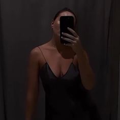 a woman taking a selfie with her phone in front of the camera and wearing a black dress