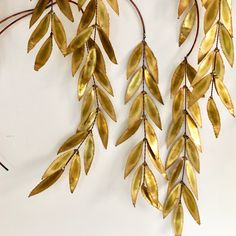 two gold leaves hang from the side of a metal wall hanging on a white wall