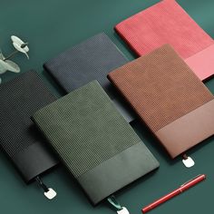 four notebooks lined up next to each other on a green surface with a red pen