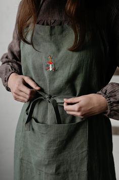 a woman in an apron is holding her hands on her hip and the other hand has a pin