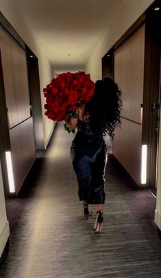 a woman walking down a long hallway with red roses in her hair and black dress