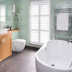 a green tiled bathroom with a white bathtub and wooden sink vanity next to a toilet