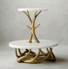 two tiered white marble cake stand with gold tree branches on each side and a round glass top