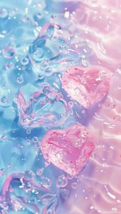 three heart shaped ice cubes floating on top of blue and pink water with bubbles