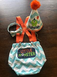 a little monster diaper, hat and lanyard are sitting on a wooden table