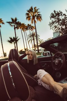 a woman sitting in the driver's seat of a car with palm trees behind her