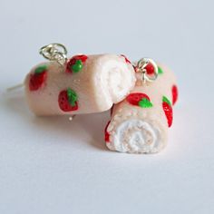 two strawberry roll necklaces are shown on a white surface, one is made out of polymer and the other has charms attached to it