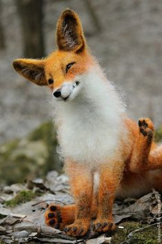 an orange and white stuffed fox sitting on top of leafy ground next to trees