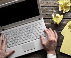 a person using a laptop computer on top of a wooden table with yellow sticky notes