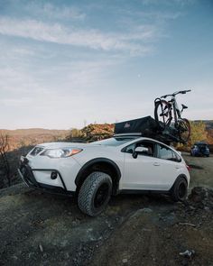 a white car parked on top of a dirt hill next to a bike mounted on it's roof