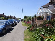 several cars parked on the side of a road next to flowers and bushes in front of a house