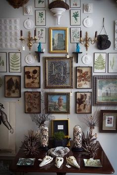 there are many framed pictures on the wall above this table with vases and other items