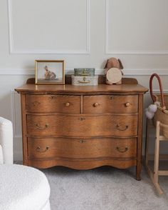 a wooden dresser sitting in a bedroom next to a white chair and teddy bear on top of it