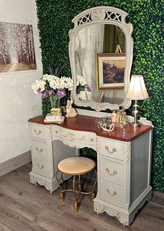 an antique vanity with mirror, stool and flowers