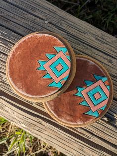 two wooden coasters with designs on them sitting on a wood table outside in the grass