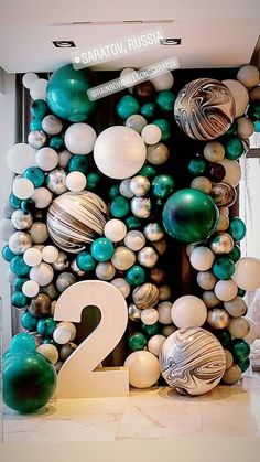 the number two is surrounded by green and white balloons in an art deco - themed room