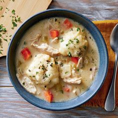 a blue bowl filled with chicken and dumplings next to a wooden spoon on top of a table