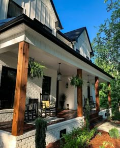 a white house with porches and rocking chairs on the front porch, surrounded by greenery