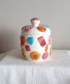 a cookie jar is sitting on top of a white towel with hearts and candies painted on it