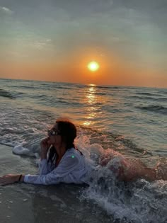 a woman laying on the beach with her feet in the water and sun setting behind her