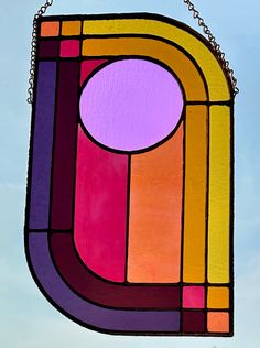 a colorful stained glass window hanging from a chain on a blue sky with clouds in the background