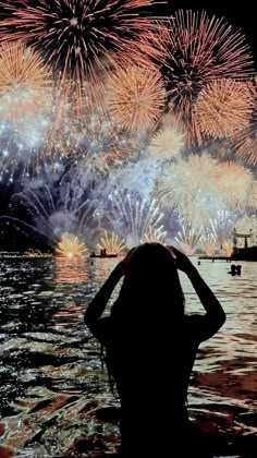 a woman standing in the water watching fireworks